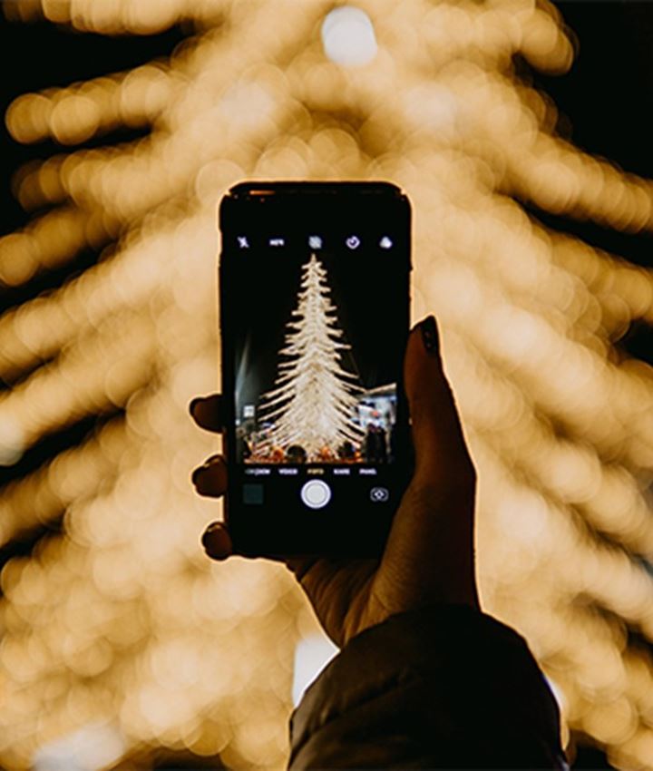 Persoon met mobiel die foto maakt van verlichte kerstboom